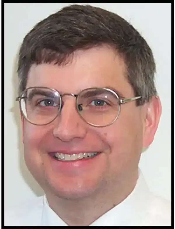 Headshot of a smiling person wearing glasses and a white shirt on a plain background