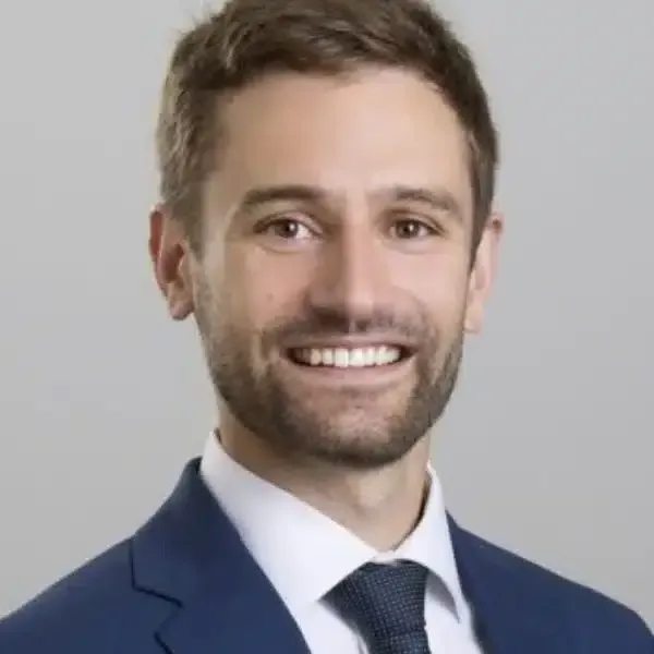 Smiling man in a blue suit and tie against a light gray background