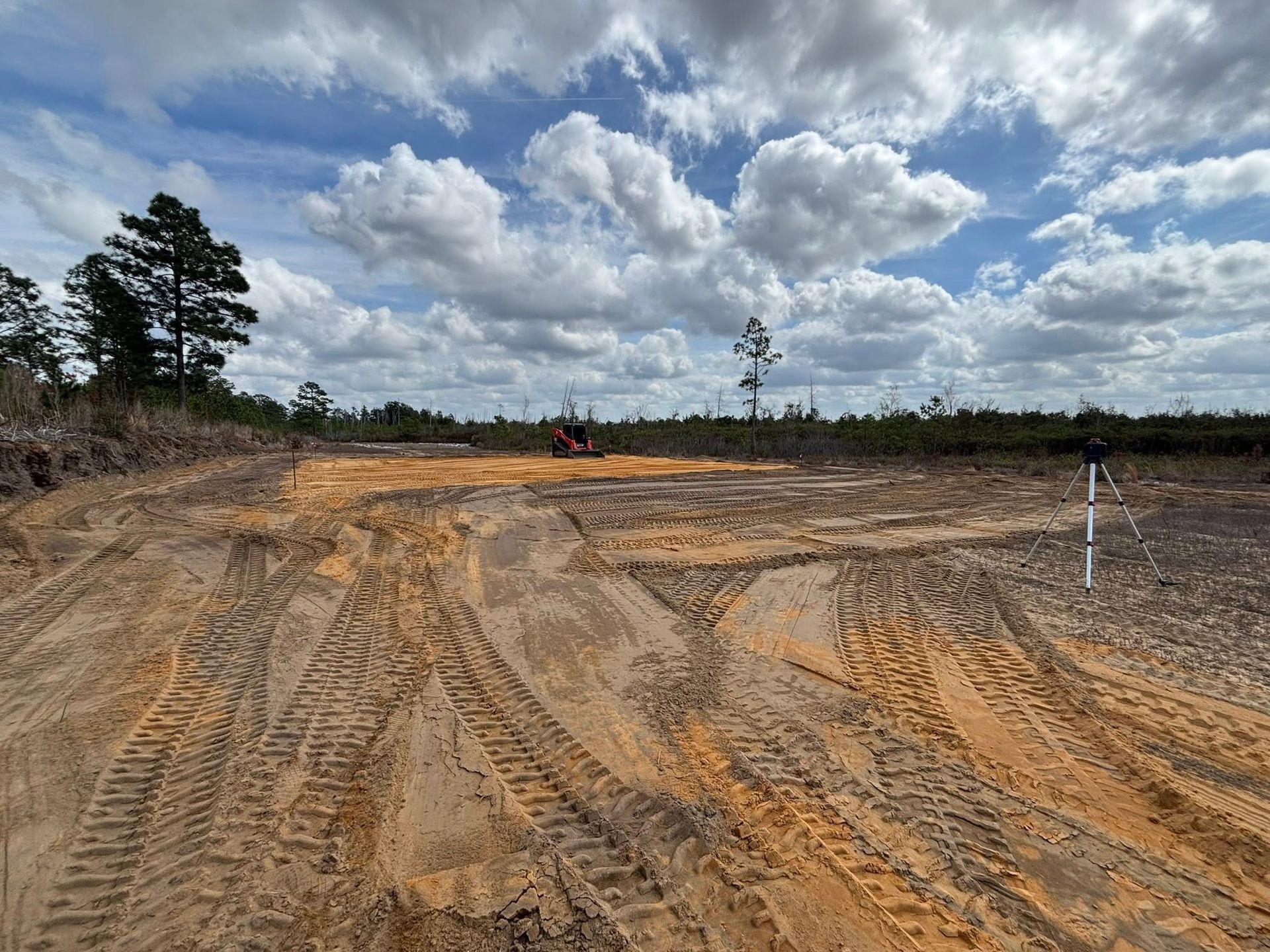 Sandy construction site with tire tracks, dirt mounds, and cloudy sky