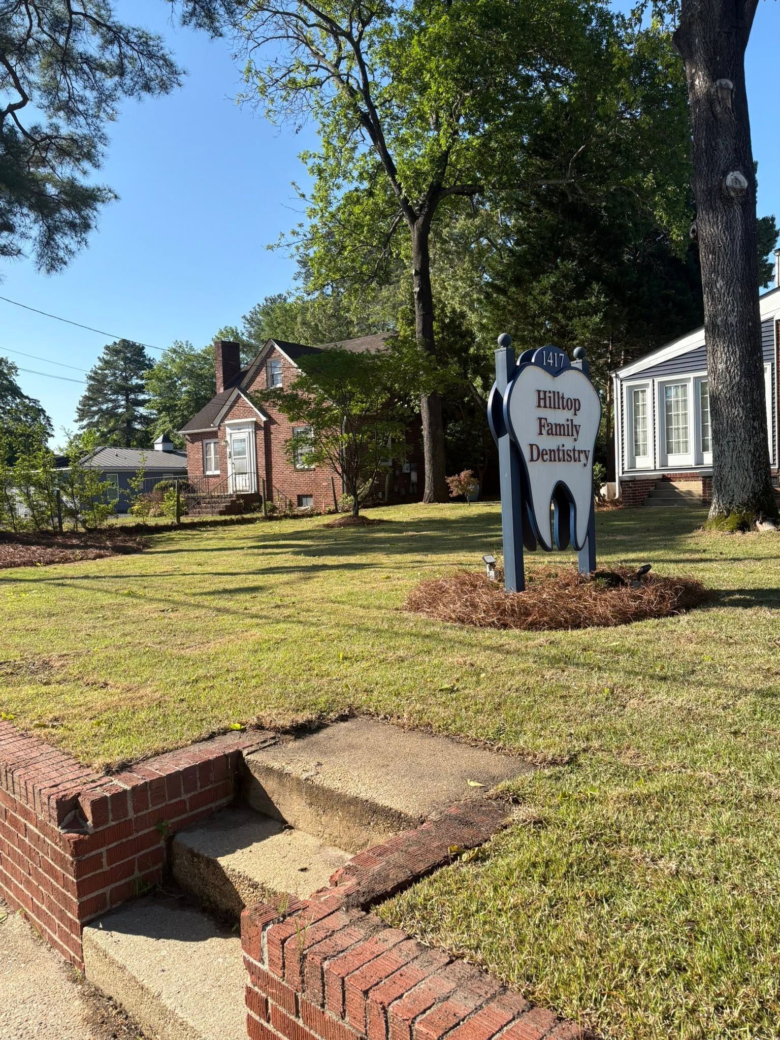 Neighborhood yard sign beside a brick walkway in front of a house, with trees and bright green grass.