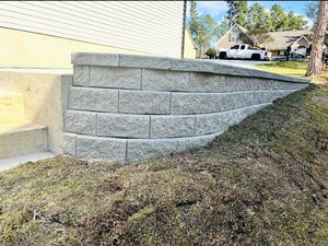 Gray stone retaining wall along a sloped grassy yard beside a house, with steps on the left