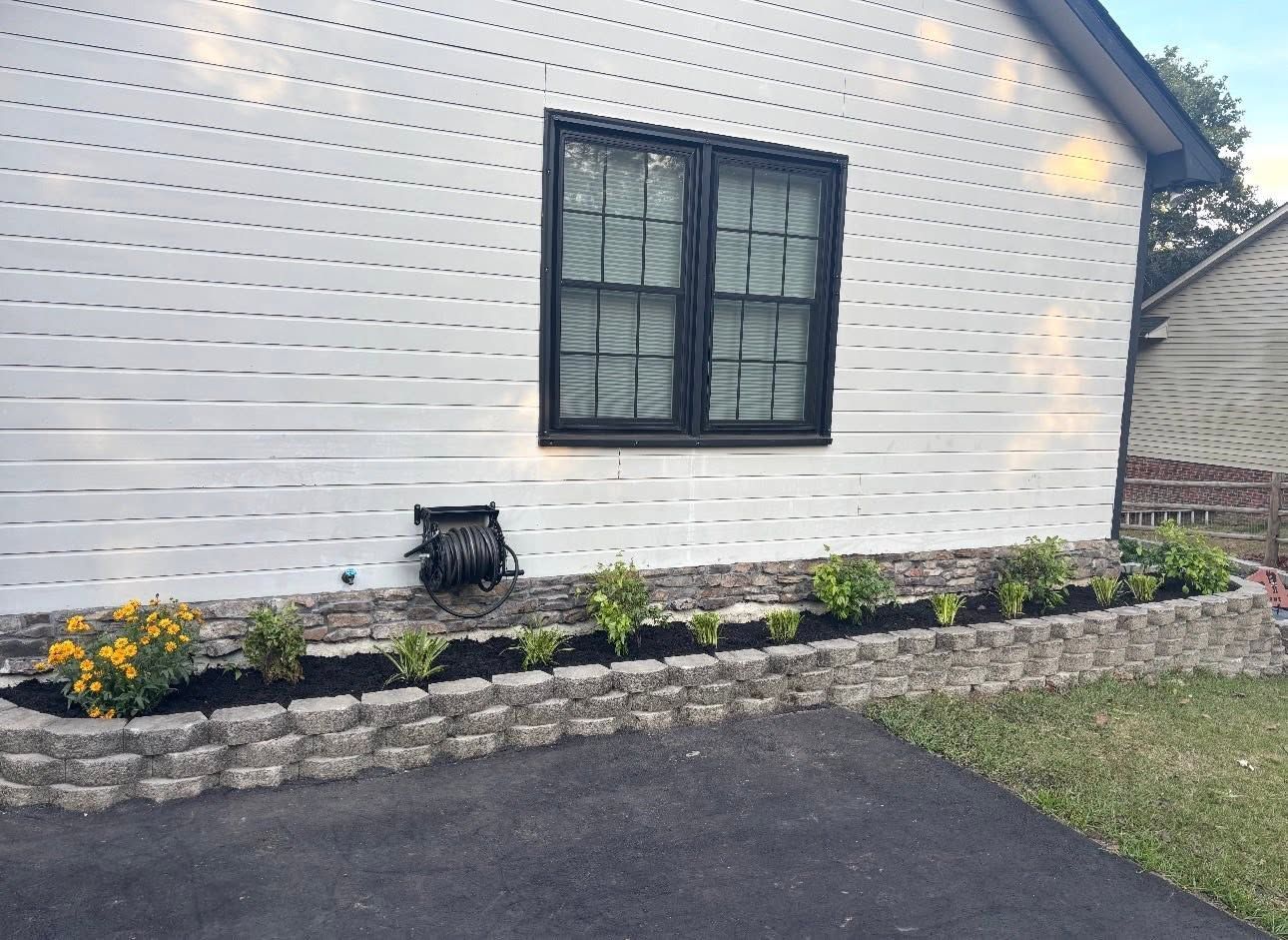 White house exterior with black window, small flower bed, and dark driveway.