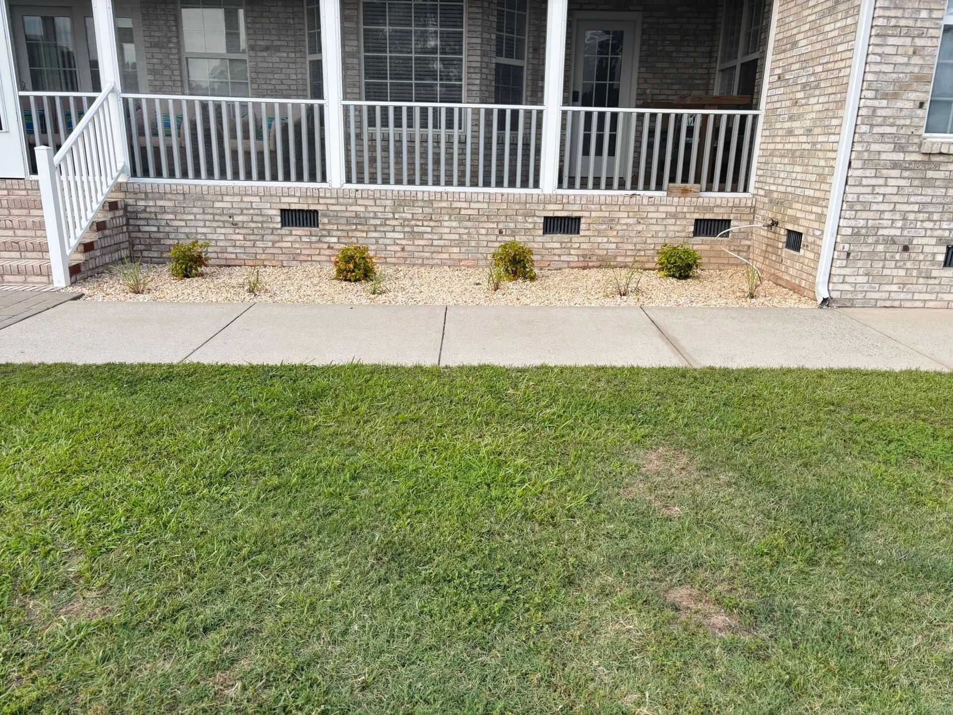 Front yard with grass, sidewalk, and a brick house porch with white railing and steps