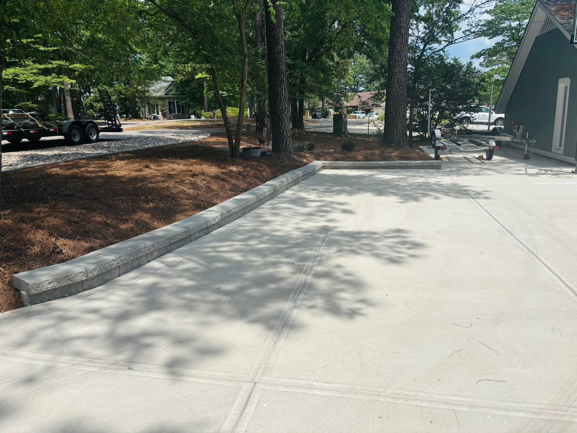 Concrete driveway beside trees and a building, with parked vehicles in the background.