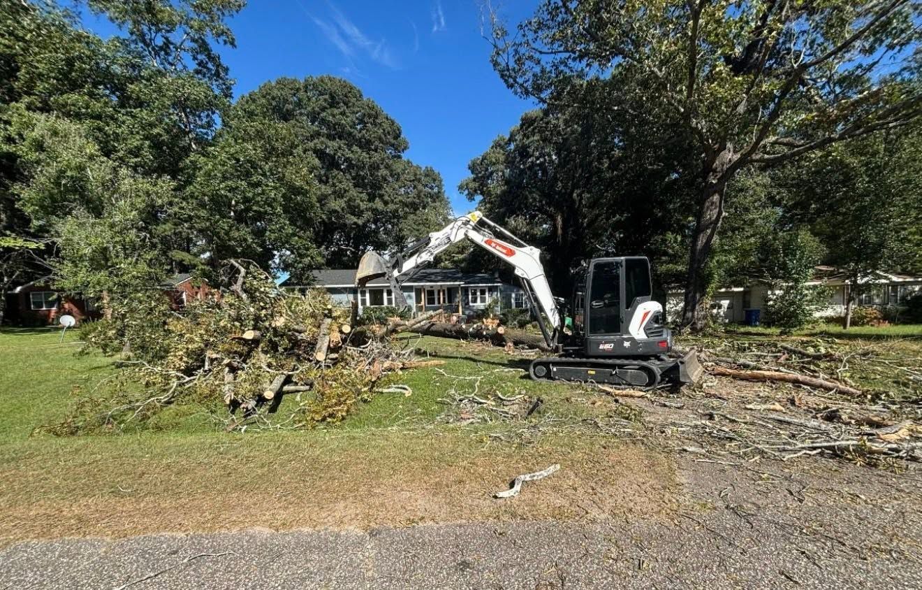 Excavator clearing storm debris in front of a house on a sunny residential street