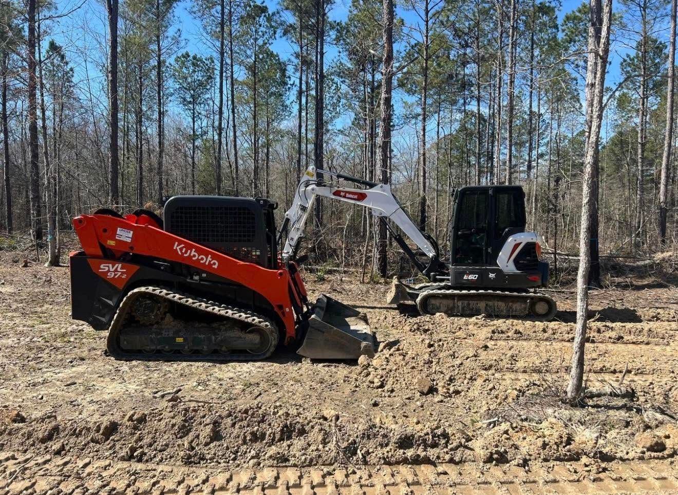 Red and white compact excavators working in a cleared wooded area under a blue sky