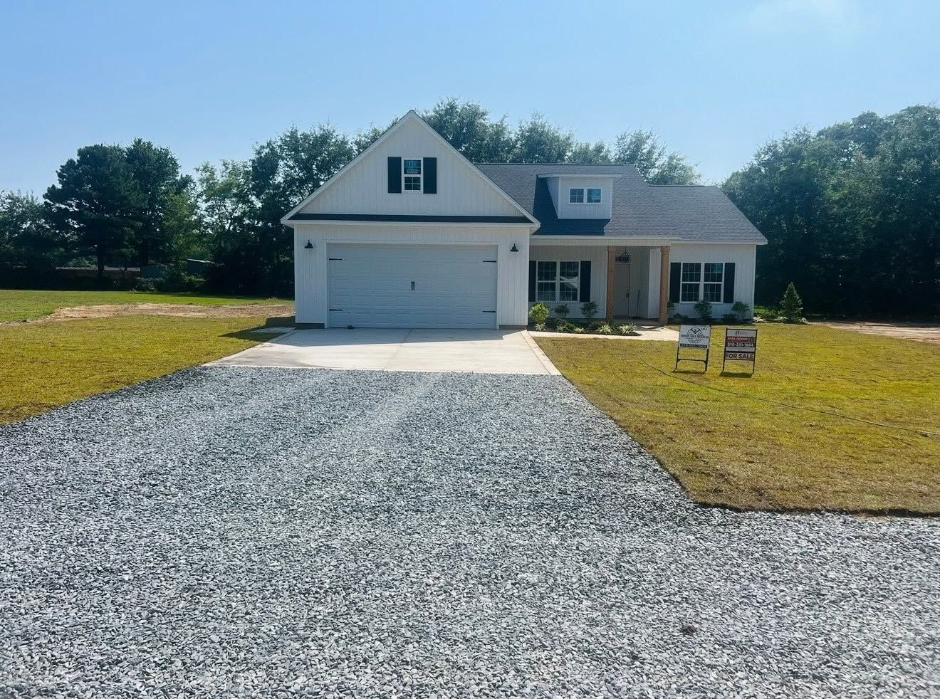White house with a garage and gravel driveway in a sunny yard