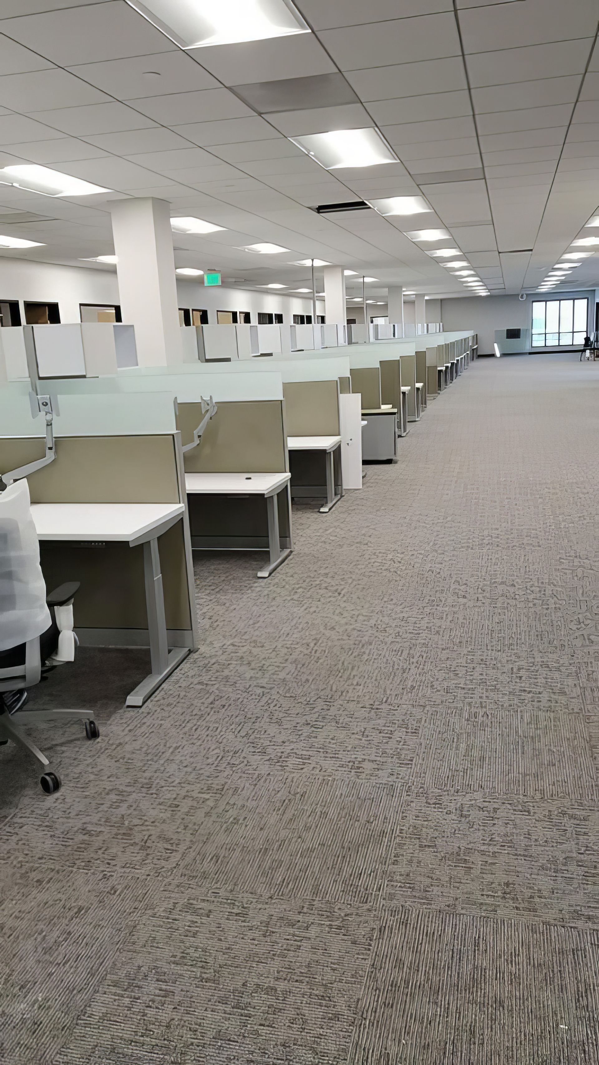 Empty office cubicle area with rows of desks under bright ceiling lights