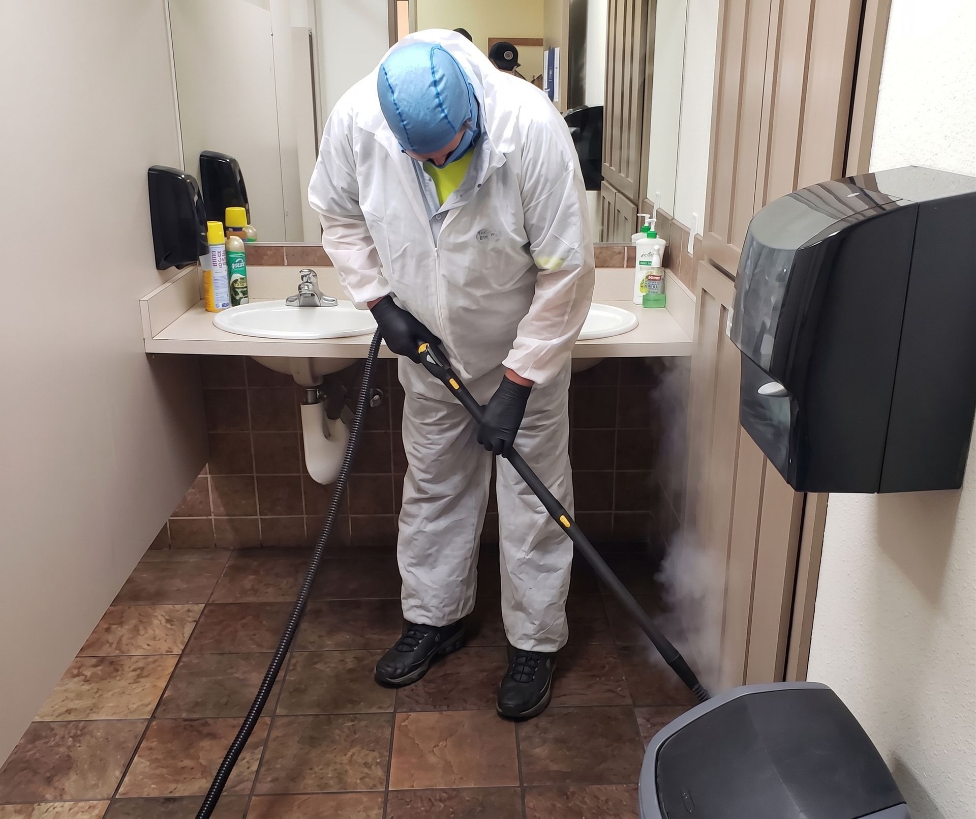 Worker in protective suit using a sprayer in a narrow indoor hallway.