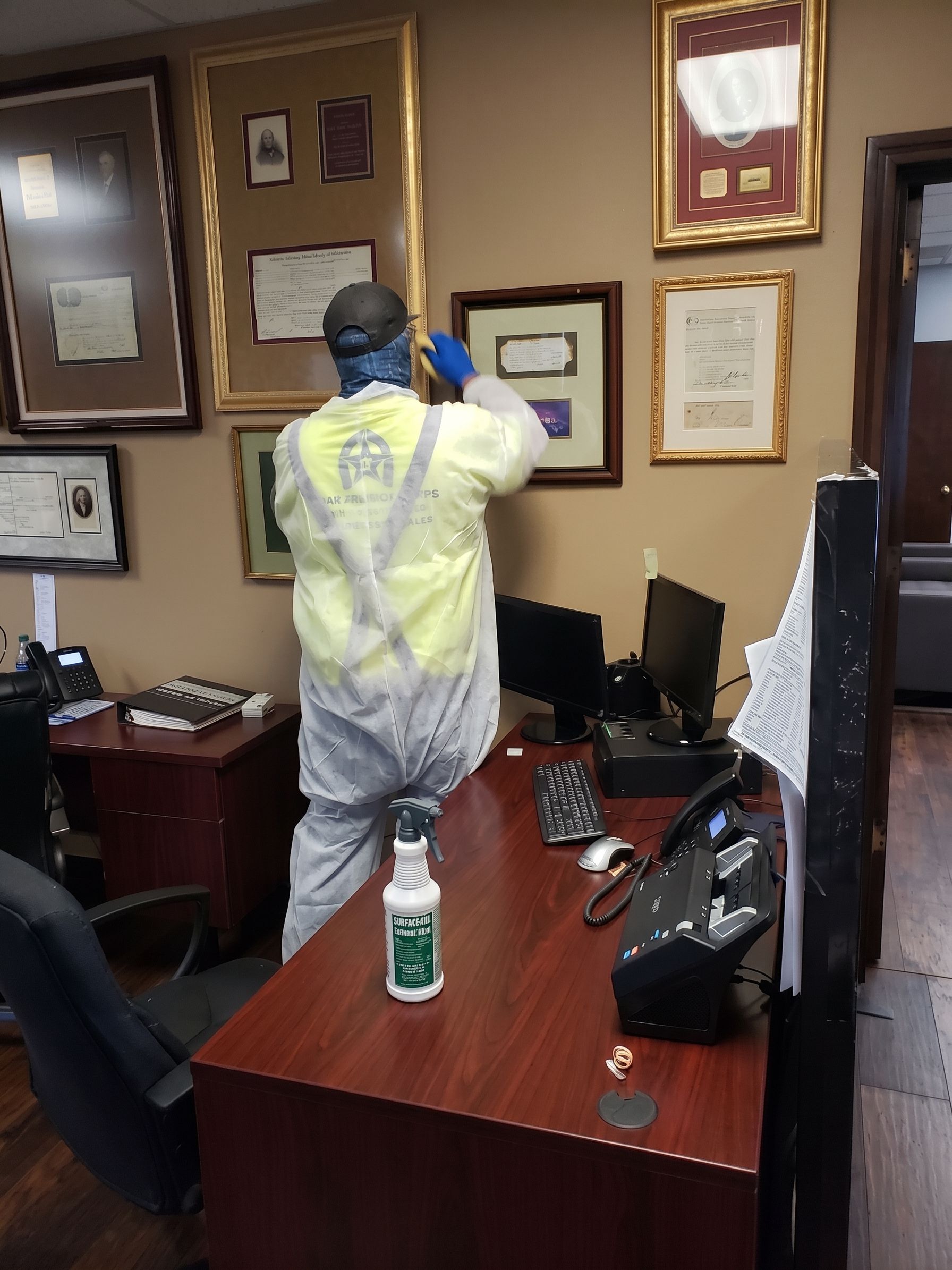 Person in a yellow protective suit hangs a framed item on an office wall.