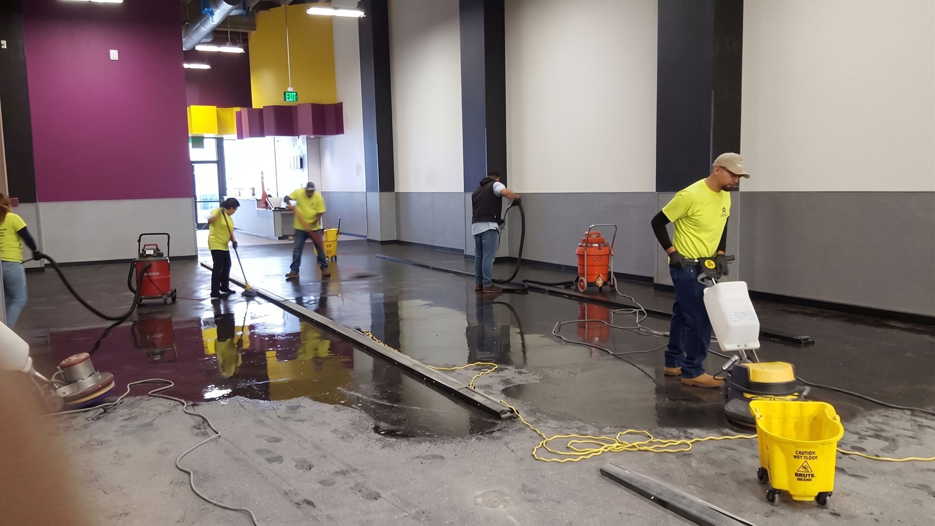 Workers cleaning a flooded indoor floor with mops, buckets, and squeegees.