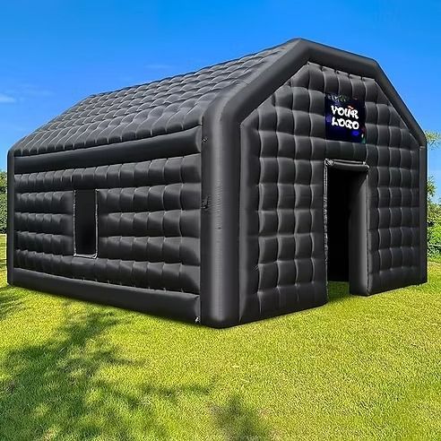 A large black inflatable tent is sitting on top of a lush green field.