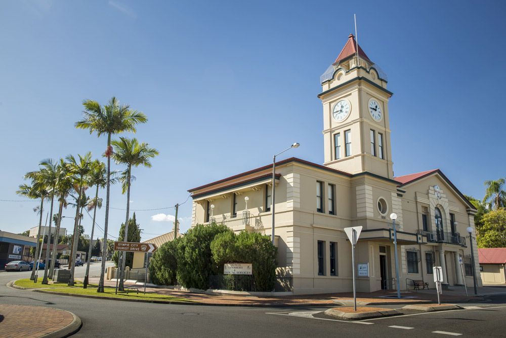 Large Building With A Clock Tower And Palm Trees In Front Of It — Builder In Gympie, QLD