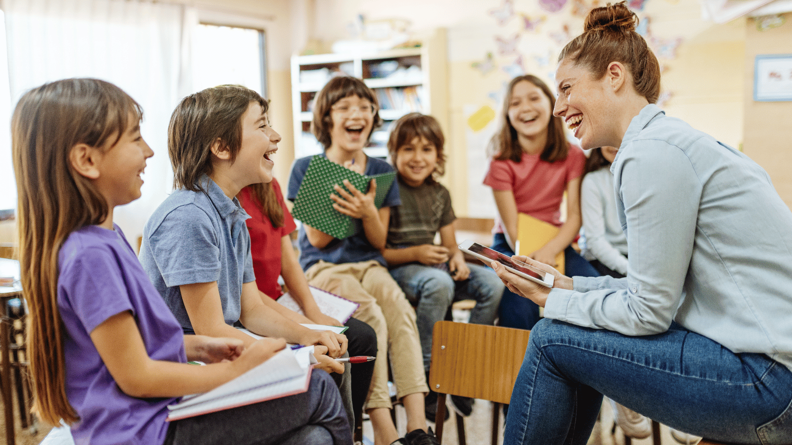 Teacher laughing with a group of students in a classroom, illustrating a welcoming school experience.