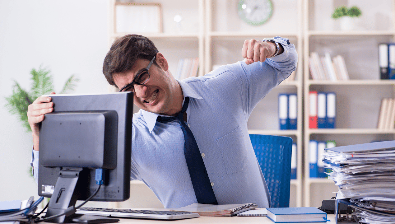 Frustrated office worker reacting to a computer beside a stack of documents, illustrating the frustration caused by long-winded writing.