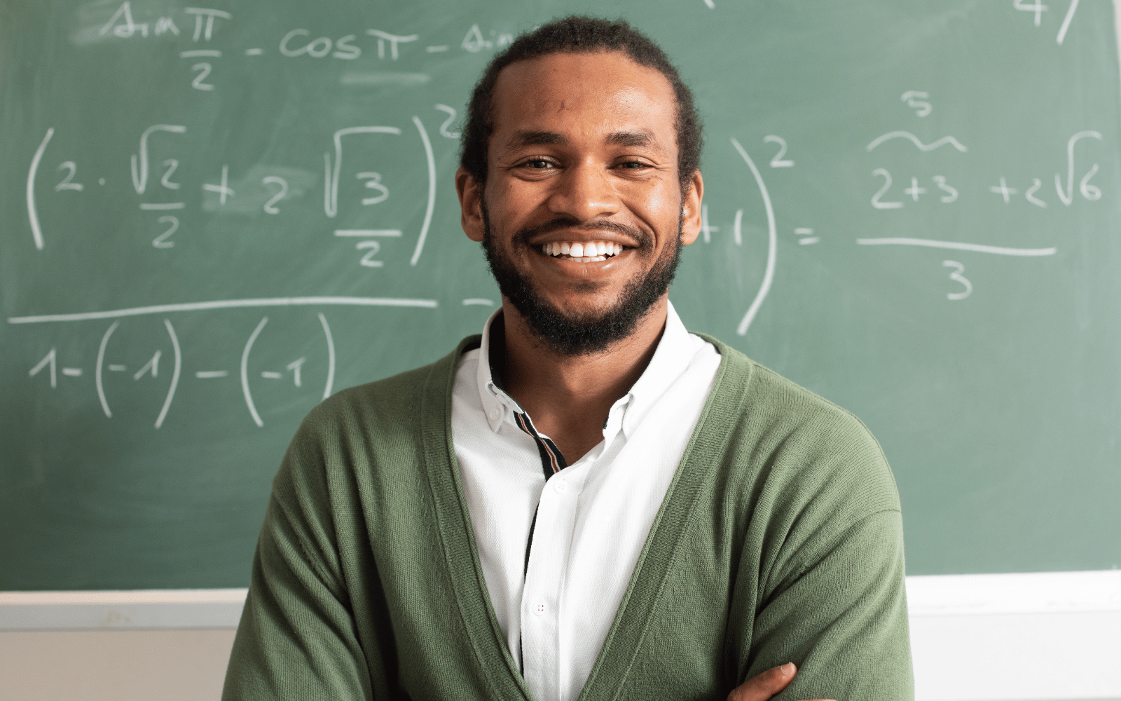 Smiling teacher standing in front of a maths chalkboard, illustrating staff profile content.