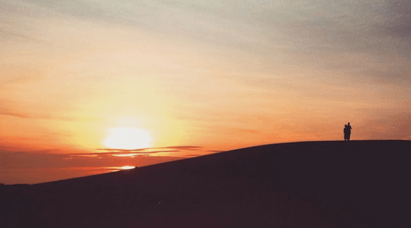 Sunset with a couple looking sand dunes, representing the reflective tone of words with deep meanings.
