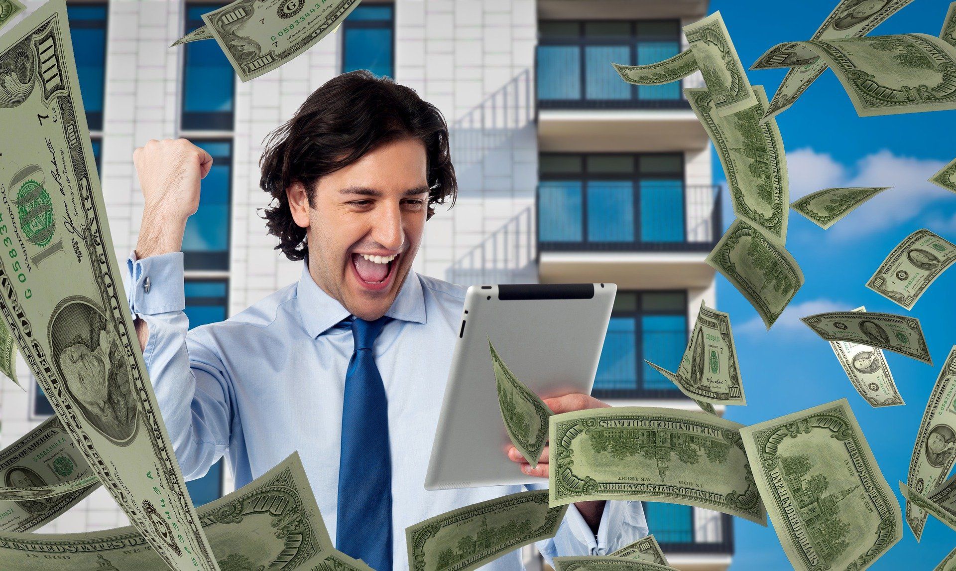 A man is holding a tablet with money falling around him