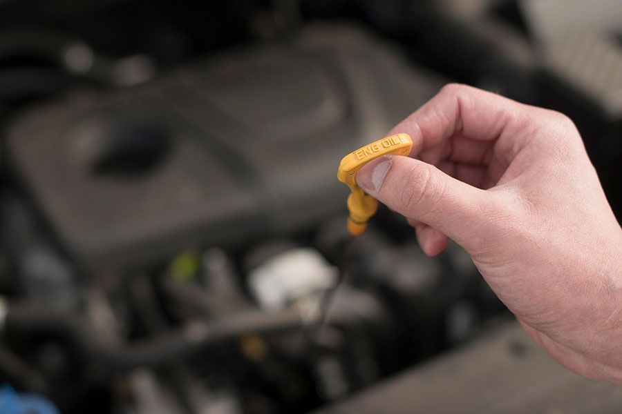 Hand holding a yellow engine oil dipstick over a car engine compartment