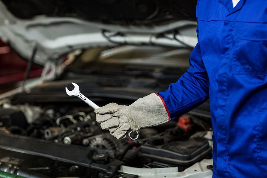 Mechanic in blue coveralls holding a wrench over an open car engine
