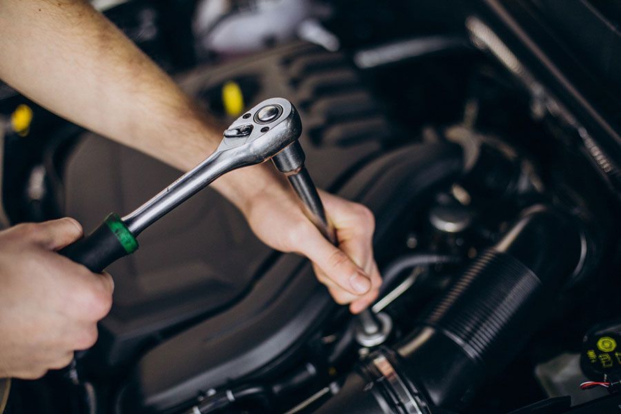 Hands using a ratchet wrench to tighten a car engine bolt in a garage