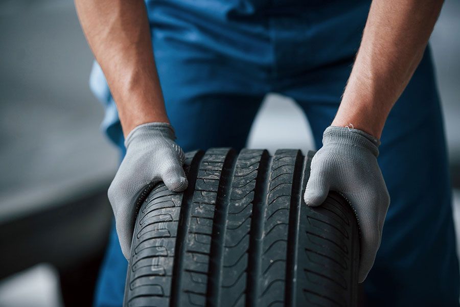 Gloved hands holding a car tire, inspecting tread in a garage-like setting