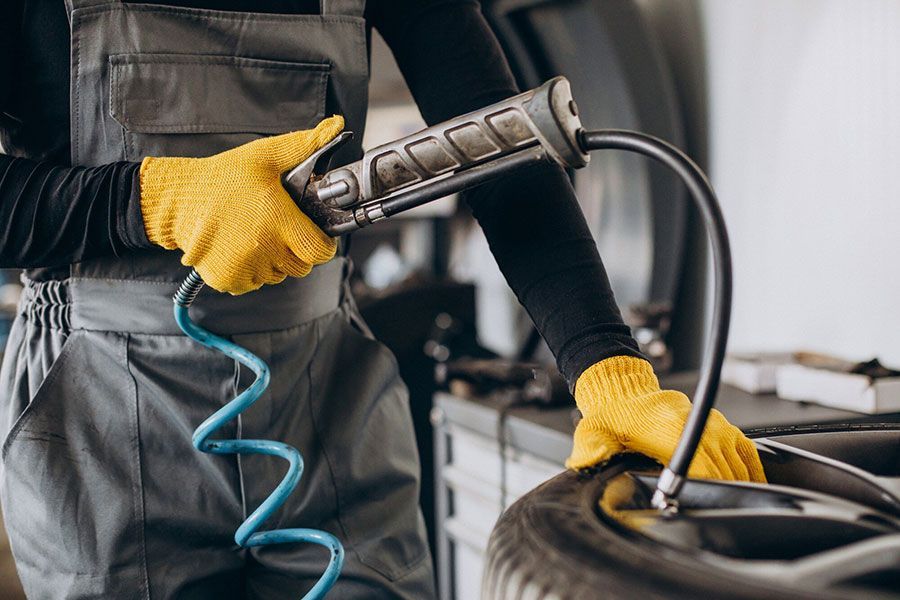 Worker using an air hose to inflate a tire in a garage, wearing yellow gloves and gray overalls
