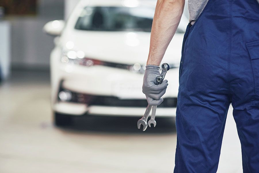 Mechanic in blue coveralls holding a wrench beside a white car in a garage