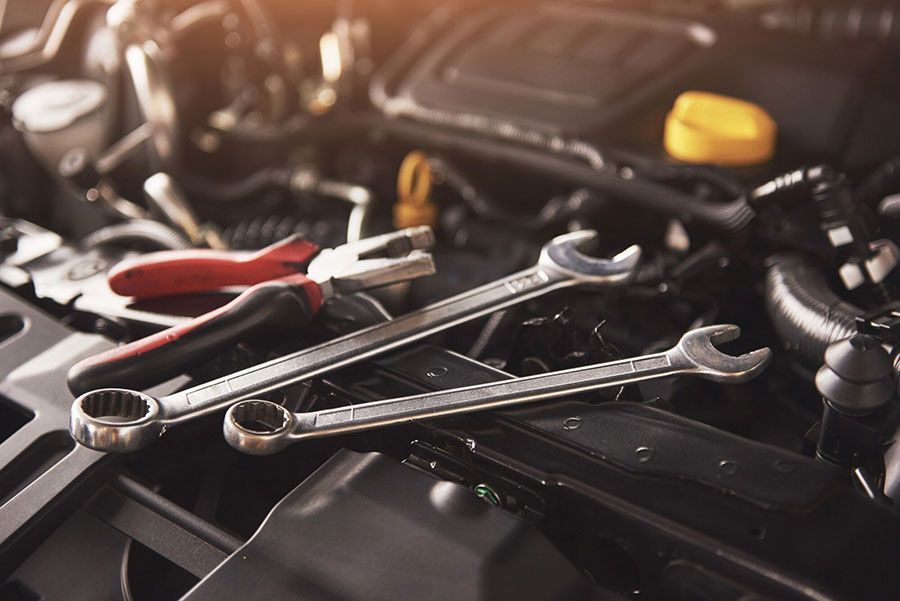 Wrenches and pliers laid across an open car engine bay, with a yellow cap in the background