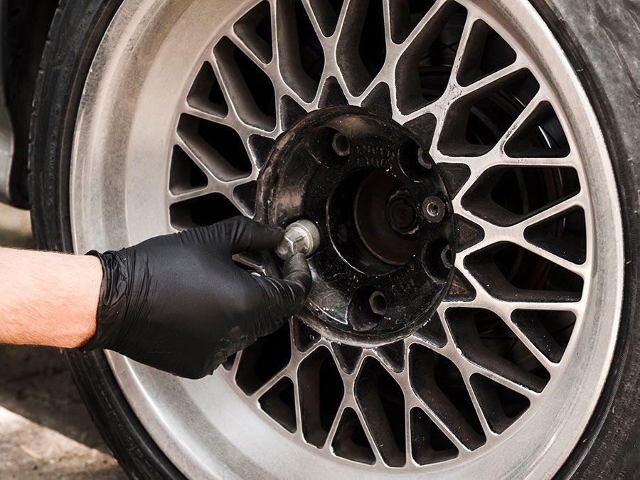 Gloved hand cleaning grease from a car wheel hub on a silver alloy rim