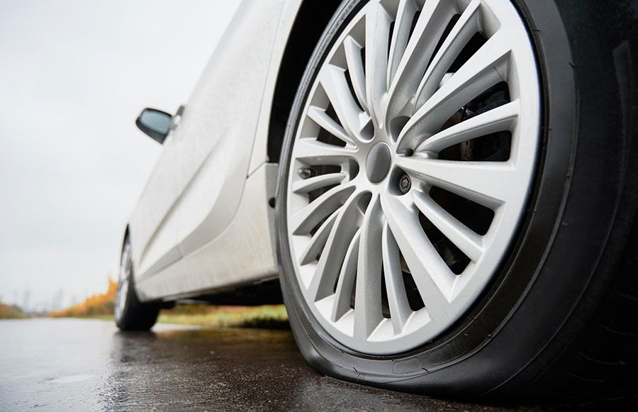 Low-angle view of a white car parked on a wet road, showing the front wheel and side body.