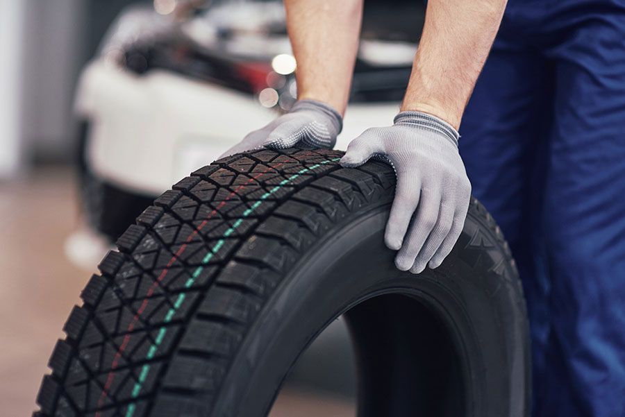 Mechanic wearing gloves holding a car tire in an auto shop