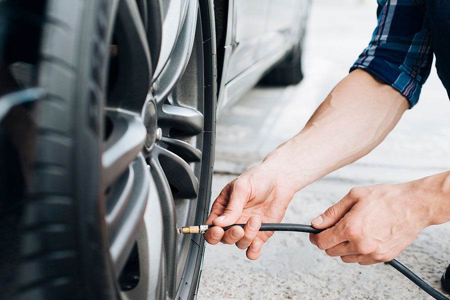 Hands inflating a car tire with a pressure gauge beside a vehicle wheel