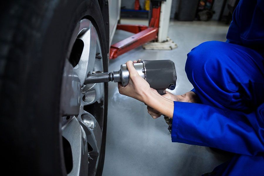Mechanic in blue coveralls using a power tool to tighten a car wheel lug nut