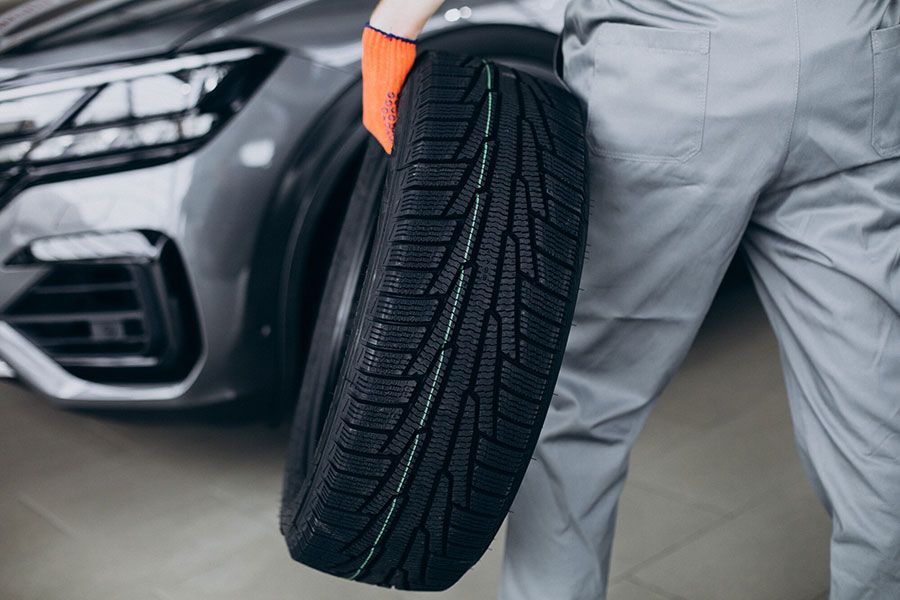 Worker holding a new tire beside a car in a garage