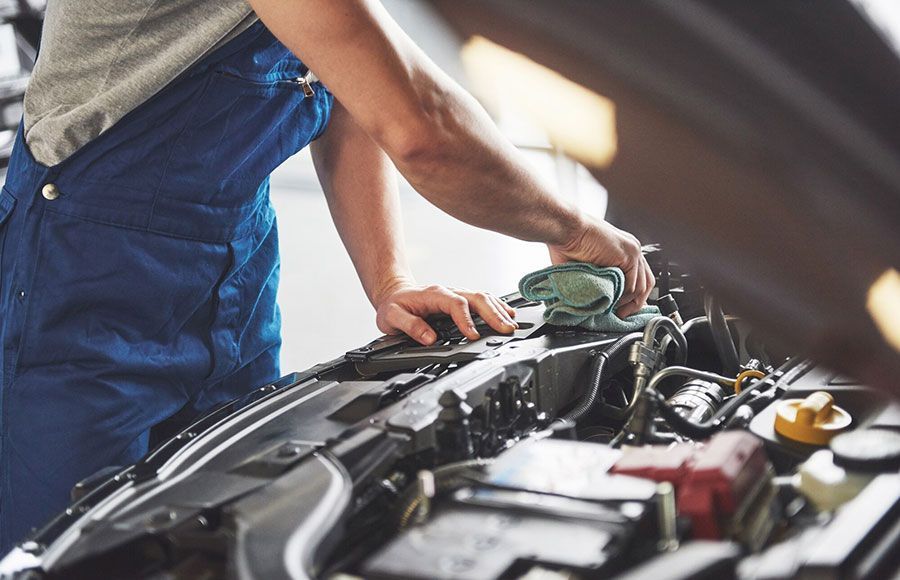 Mechanic in blue overalls working under an open car hood in a garage