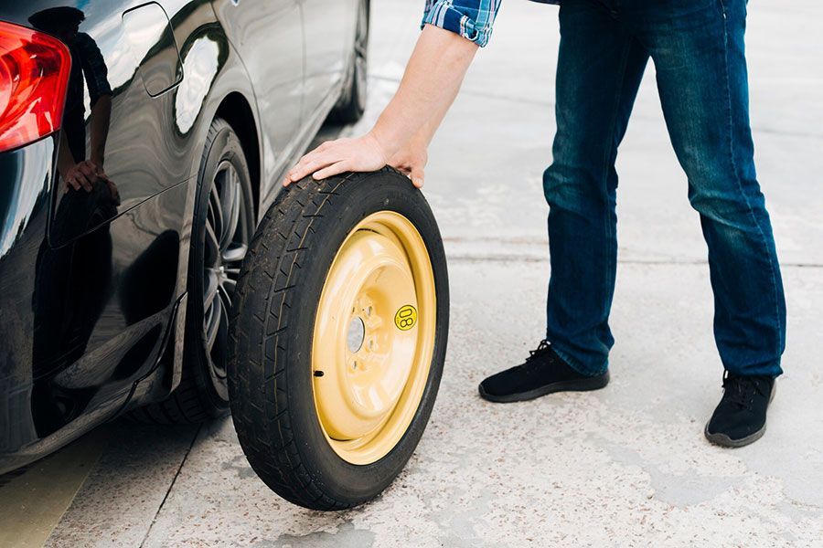 Person installing a yellow spare tire on a black car on a driveway