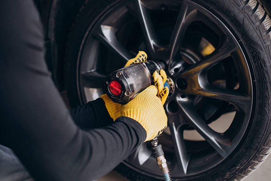 Mechanic in blue coveralls using a power tool to tighten a car wheel lug nut
