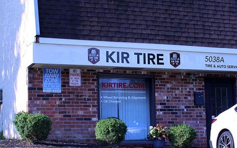 KIR Tire storefront with brick facade, blue door, and parked white vehicle at right.