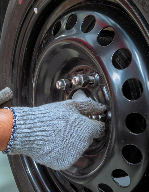 Gloved hand tightening a lug nut on a black steel car wheel