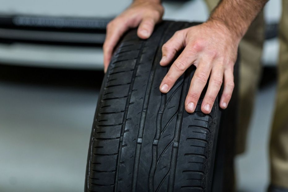 Hands inspecting a worn car tire tread in a garage