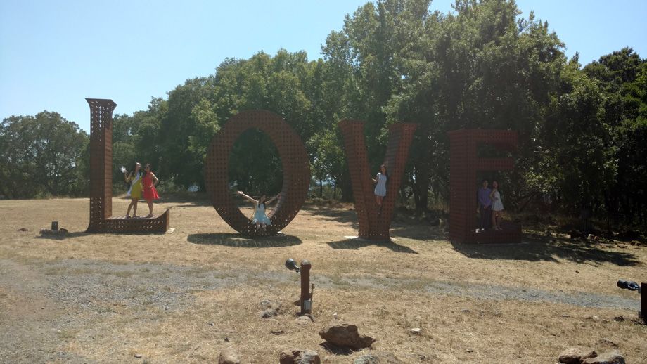 Brick “LOVE” sculpture in a sunny park with trees and a person nearby