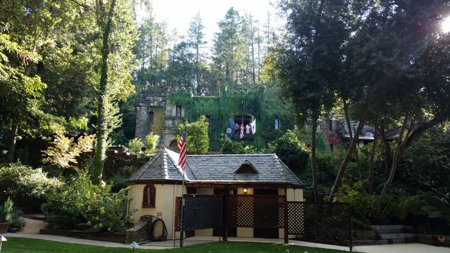 Small cottage in a wooded park with people on a balcony and a lamppost in front