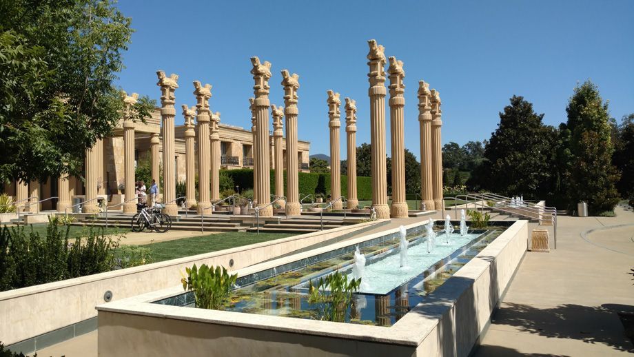 Ancient stone columns beside a long reflecting pool in a sunny garden courtyard