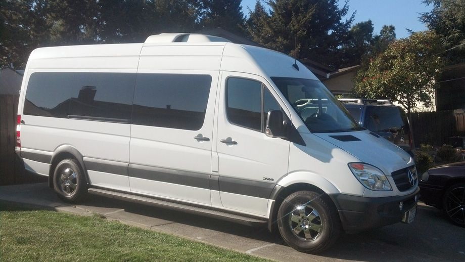 White passenger van parked on a street beside grass and trees on a sunny day