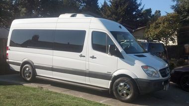 White passenger van parked on a sunny street beside grass and trees