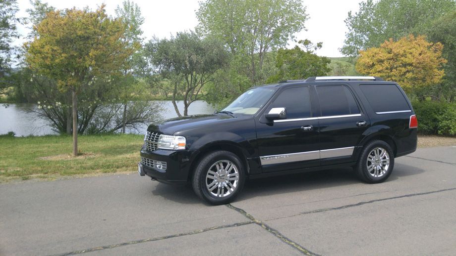 Black SUV parked on a roadside beside trees and water under an overcast sky