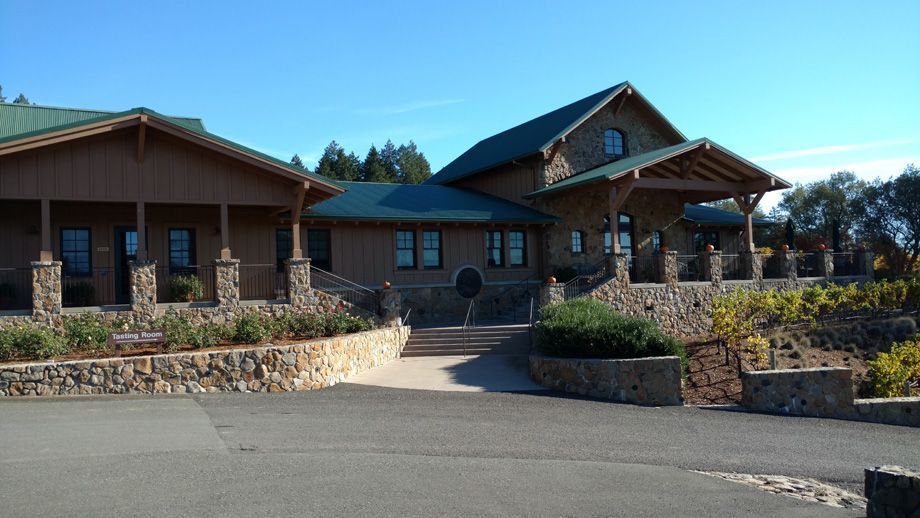 Rustic lodge-style building with stone landscaping and a paved driveway under a clear blue sky