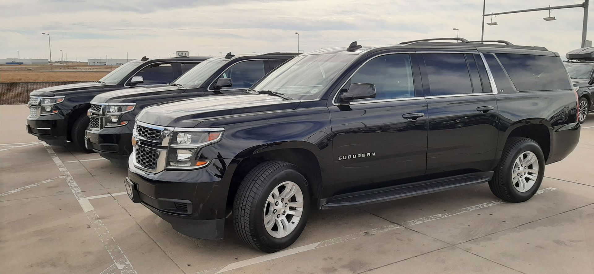 Dark SUV parked in a row of vehicles on a concrete lot under an overcast sky