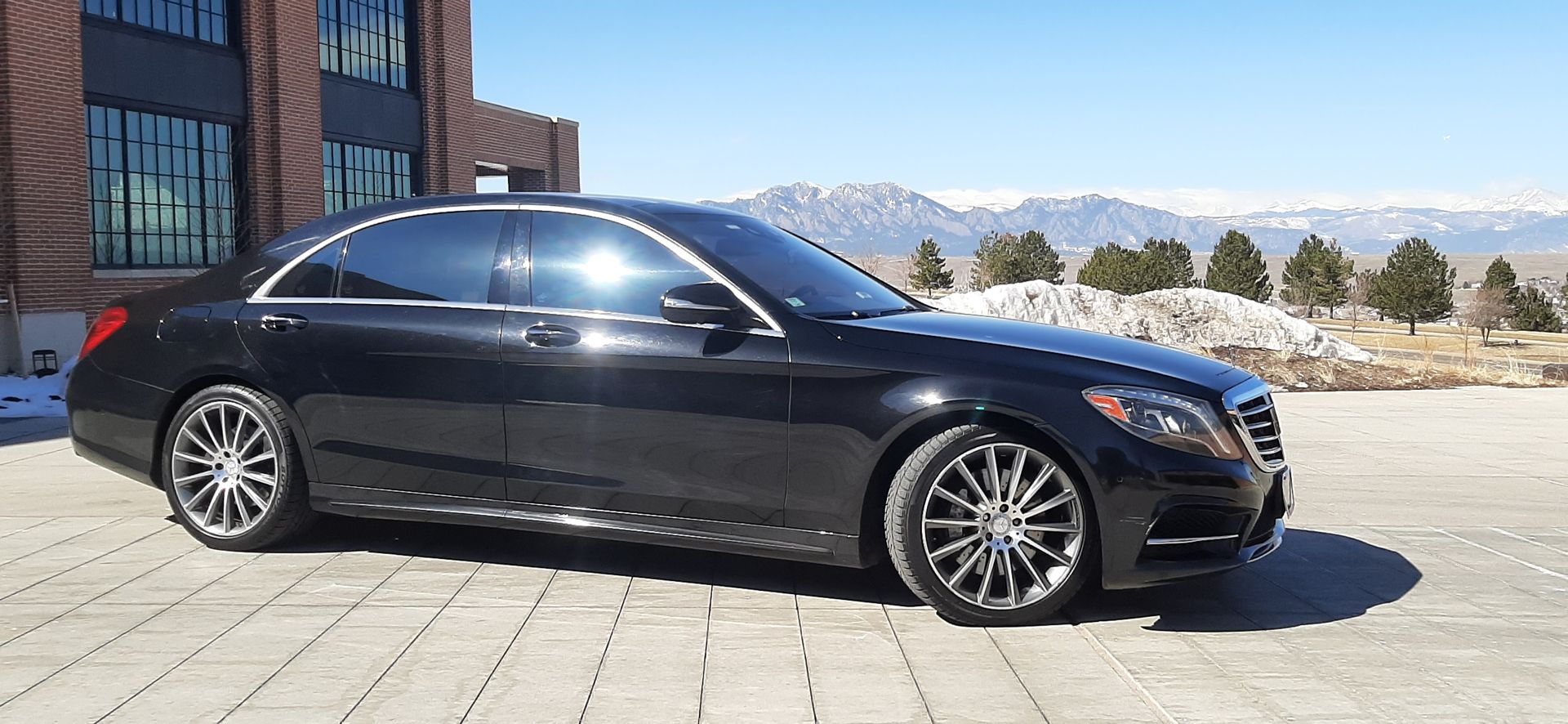 Black luxury sedan parked on a paved lot beside a modern building on a sunny day
